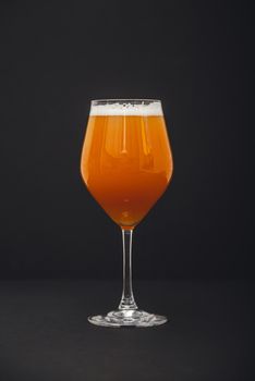 A tulip glass filled with craft beer displaying a rich amber color and frothy head against a dark background.