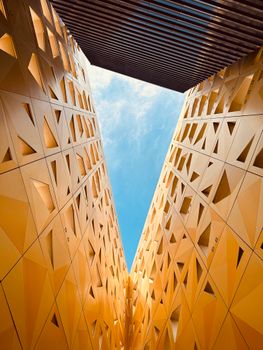 Upward view of modern architectural structures with geometric patterns against a clear sky.