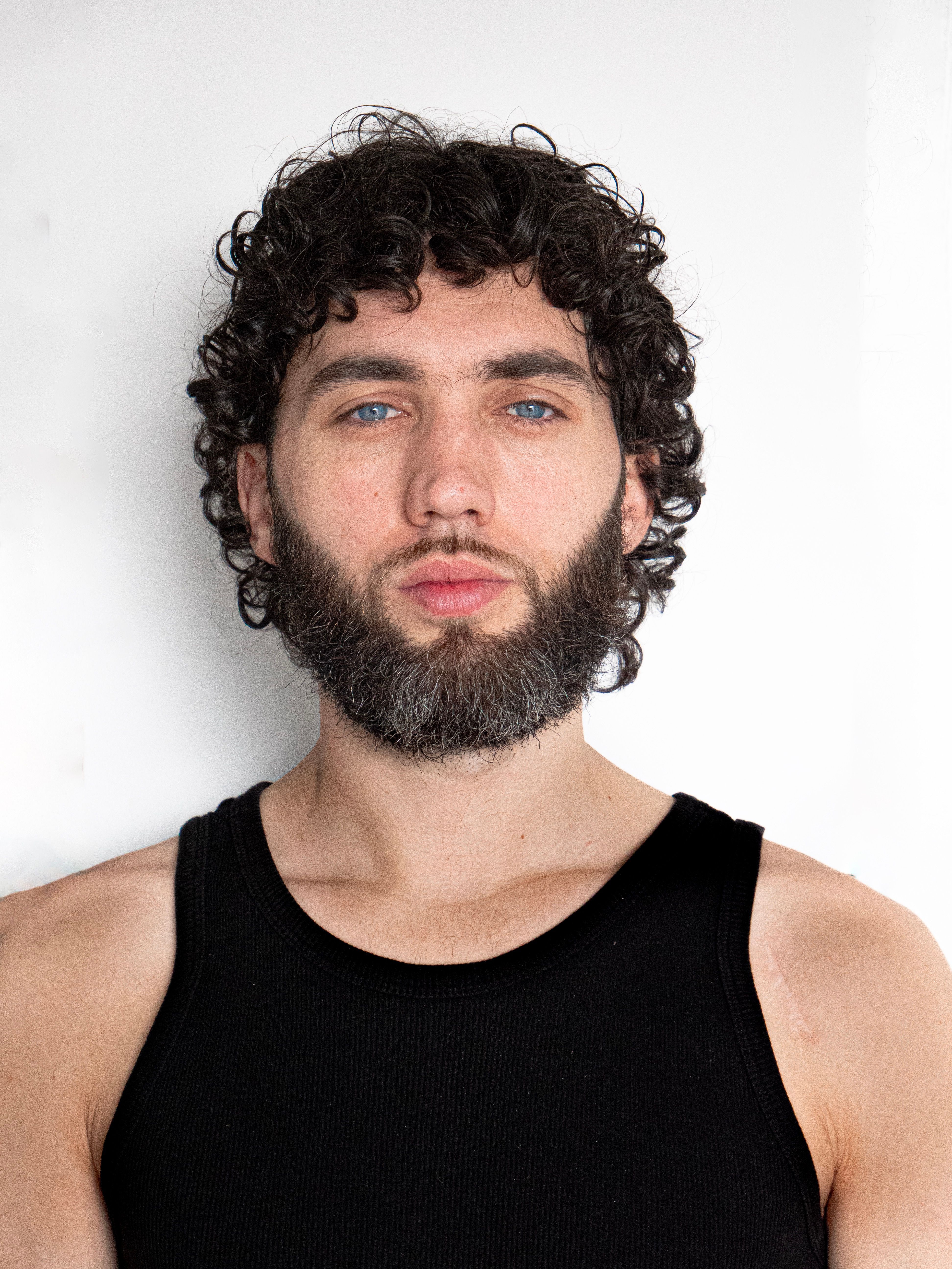 Close-up portrait of a bearded man with curly hair wearing a black tank top.