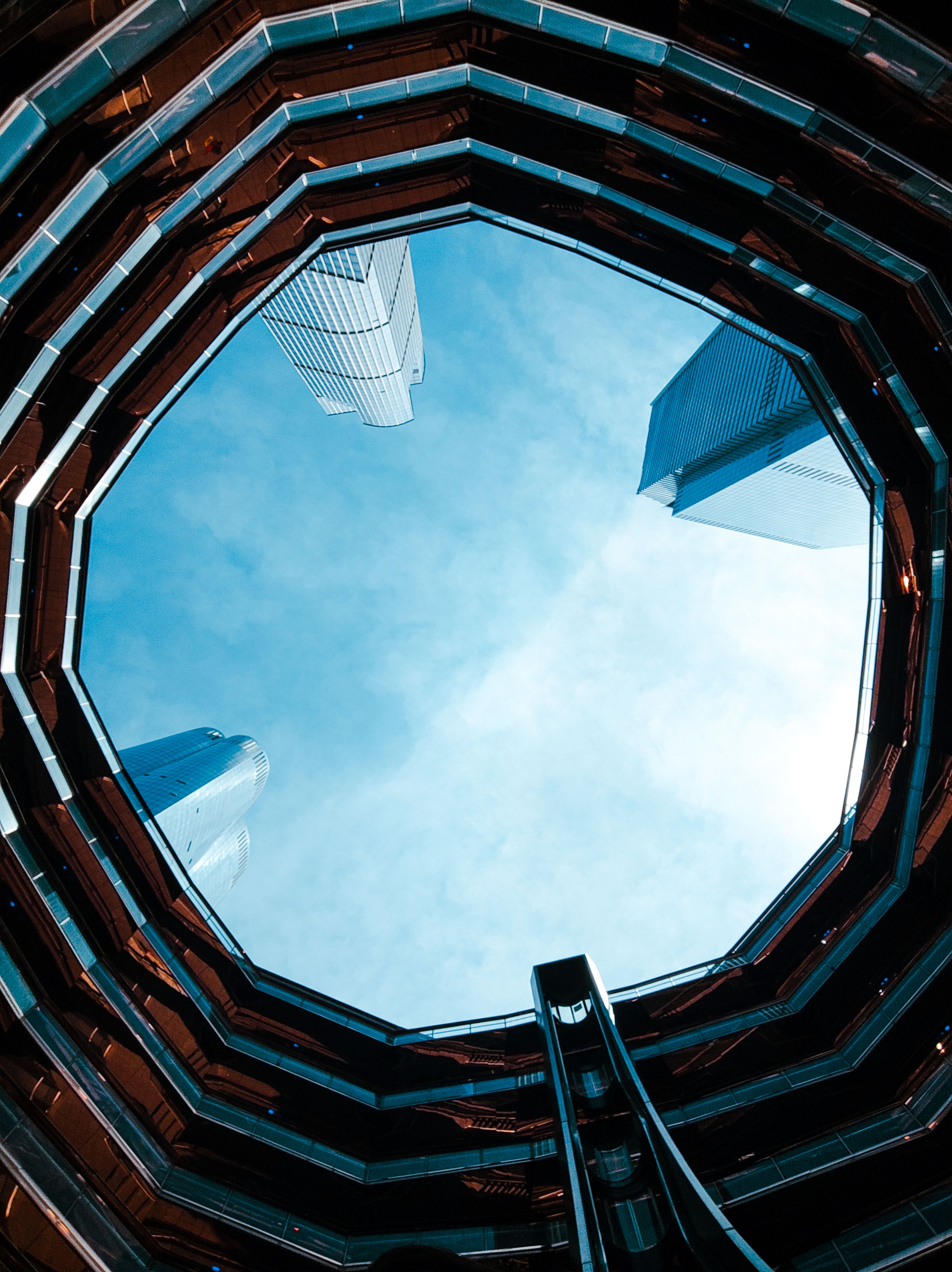 A stunning upward view from inside The Vessel, showcasing modern NYC architecture against a clear sky.