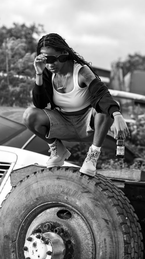 Free Black and white portrait of a woman confidently posing on a large truck tire outdoors. Stock Photo
