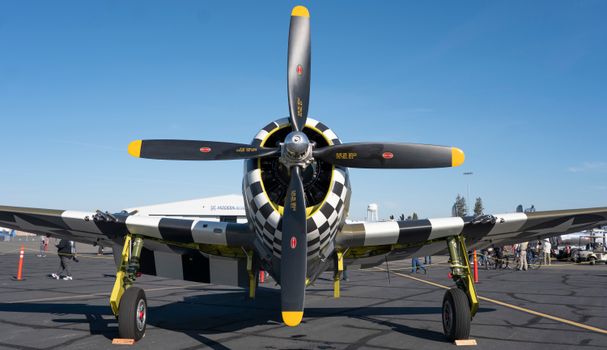 Front view of a vintage fighter plane with checkered nose at an outdoor airshow.
