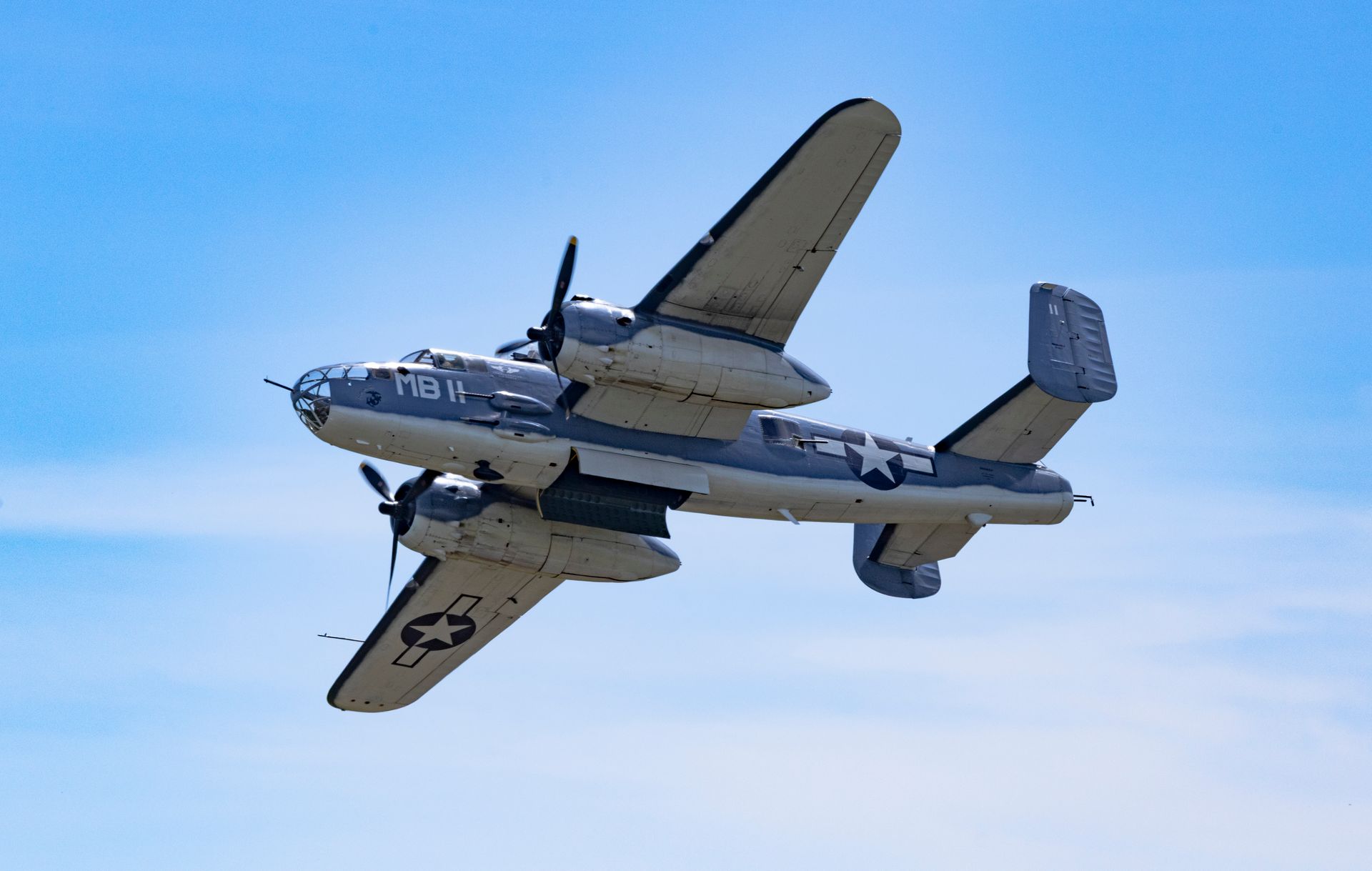 A vintage World War II B-25 Mitchell bomber flying under clear skies, showcasing historic aviation.