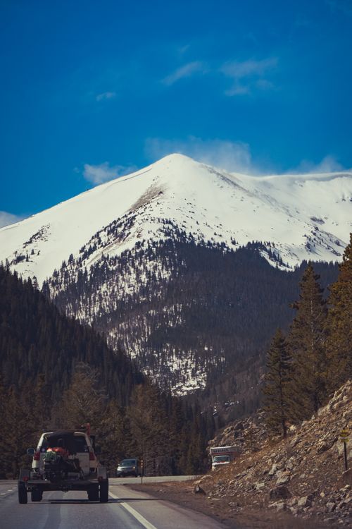 Free Cars travel on a highway through stunning snow-capped mountains, perfect for adventure enthusiasts. Stock Photo