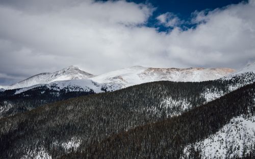 Free Breathtaking view of snow-capped mountains with dense forest beneath cloudy skies. Stock Photo
