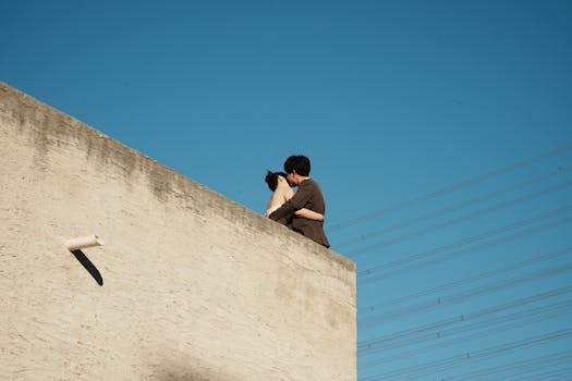 A couple embraces on a rooftop against a clear blue sky, capturing a romantic moment.