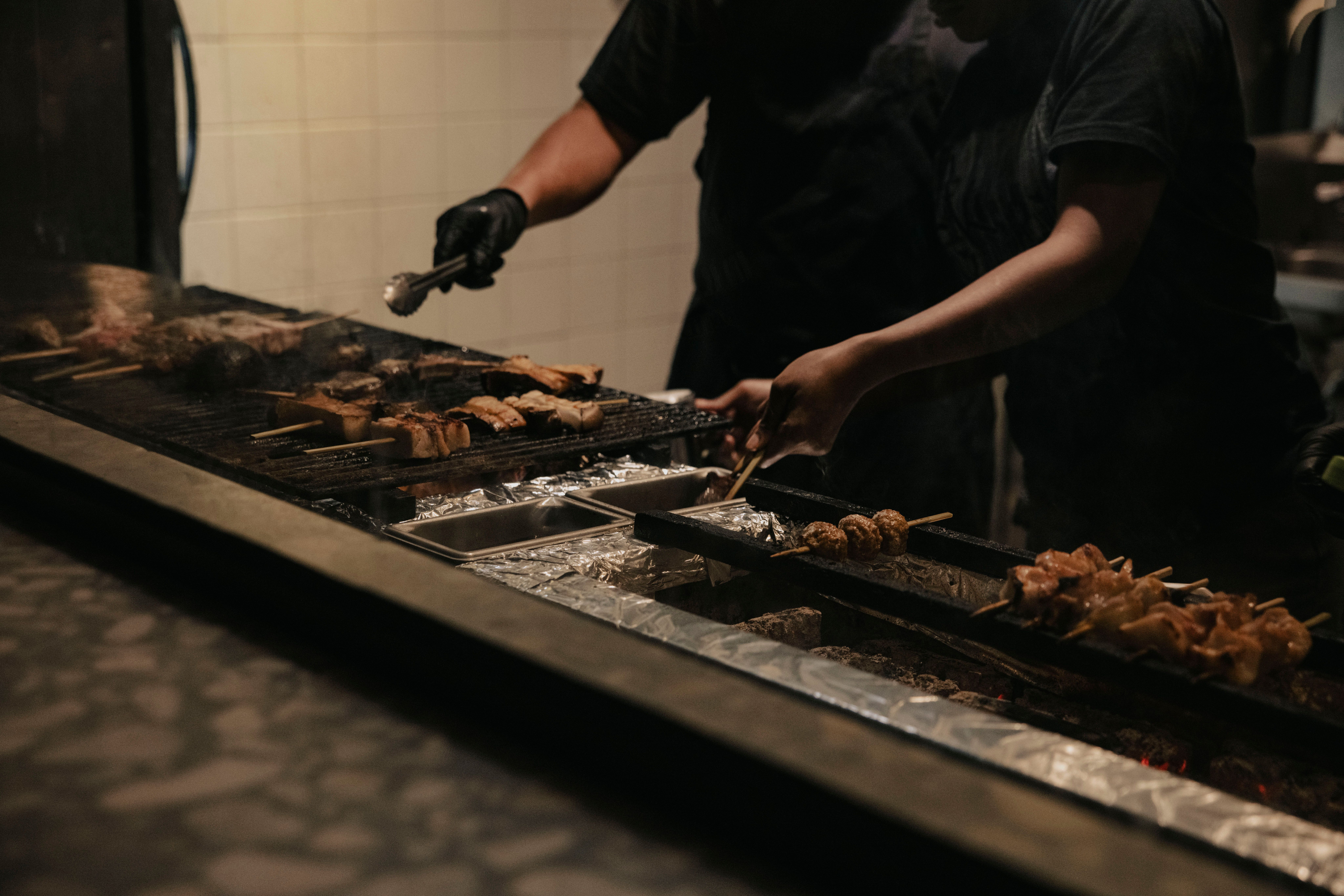 Deux cuisiniers retournant des brochettes le long d'un grand gril à charbon, vue large