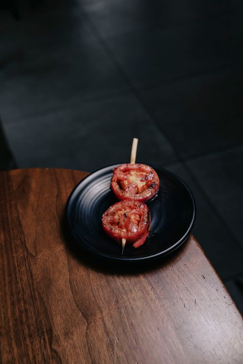 Free A beautifully grilled tomato skewer served on a black plate, emphasizing rustic presentation. Stock Photo