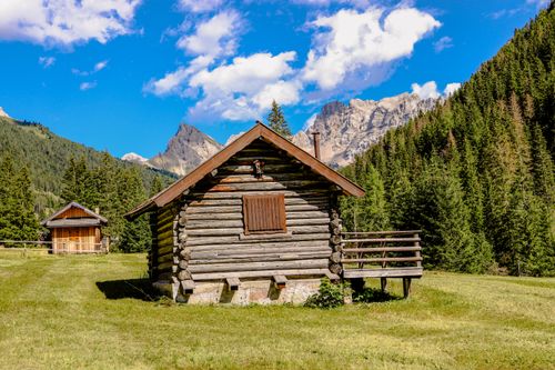 Free Log cabin in sunny mountain landscape with blue skies and pine trees. Stock Photo