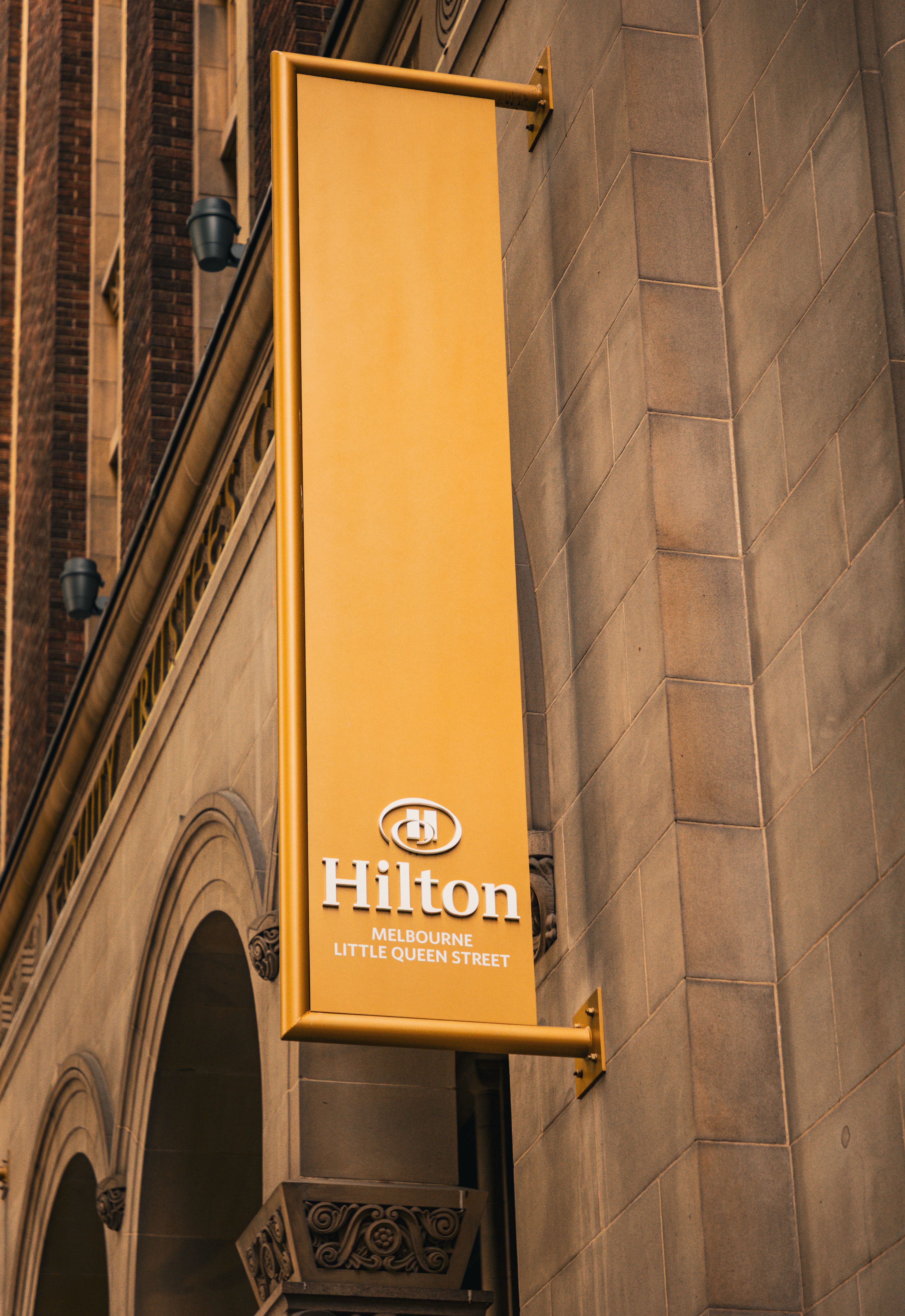 A vertical yellow Hilton Hotel sign on a historic building in Melbourne, Australia.