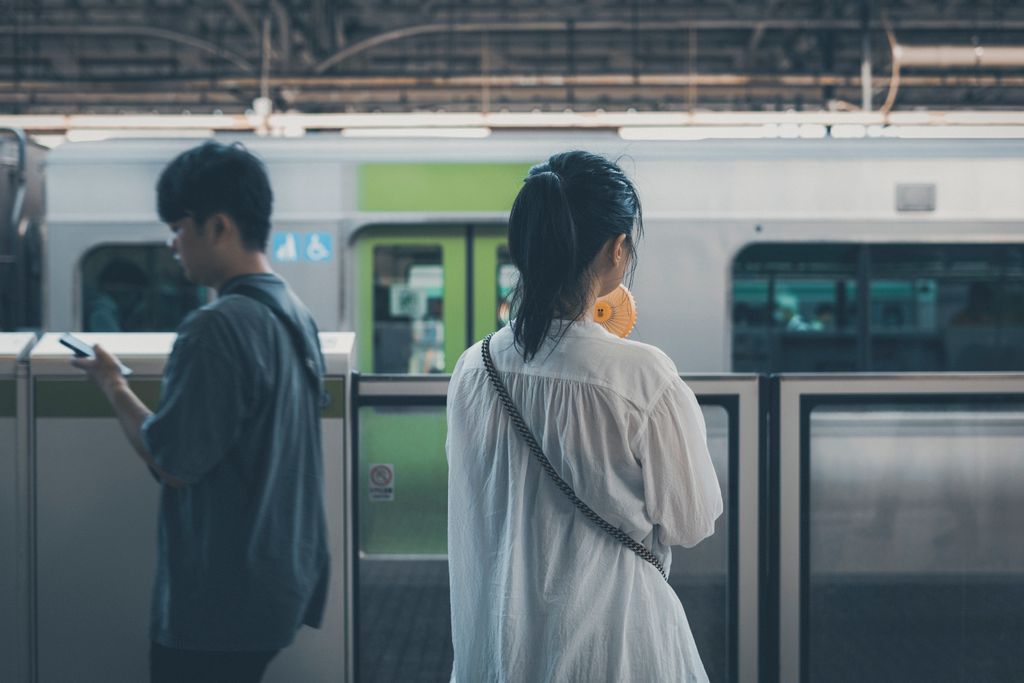 Two people waiting at a Tokyo train station platform, capturing the essence of urban commuting.