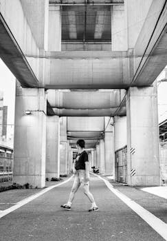 Black and white photo of a pedestrian under an urban concrete structure in Tokyo, Japan.
