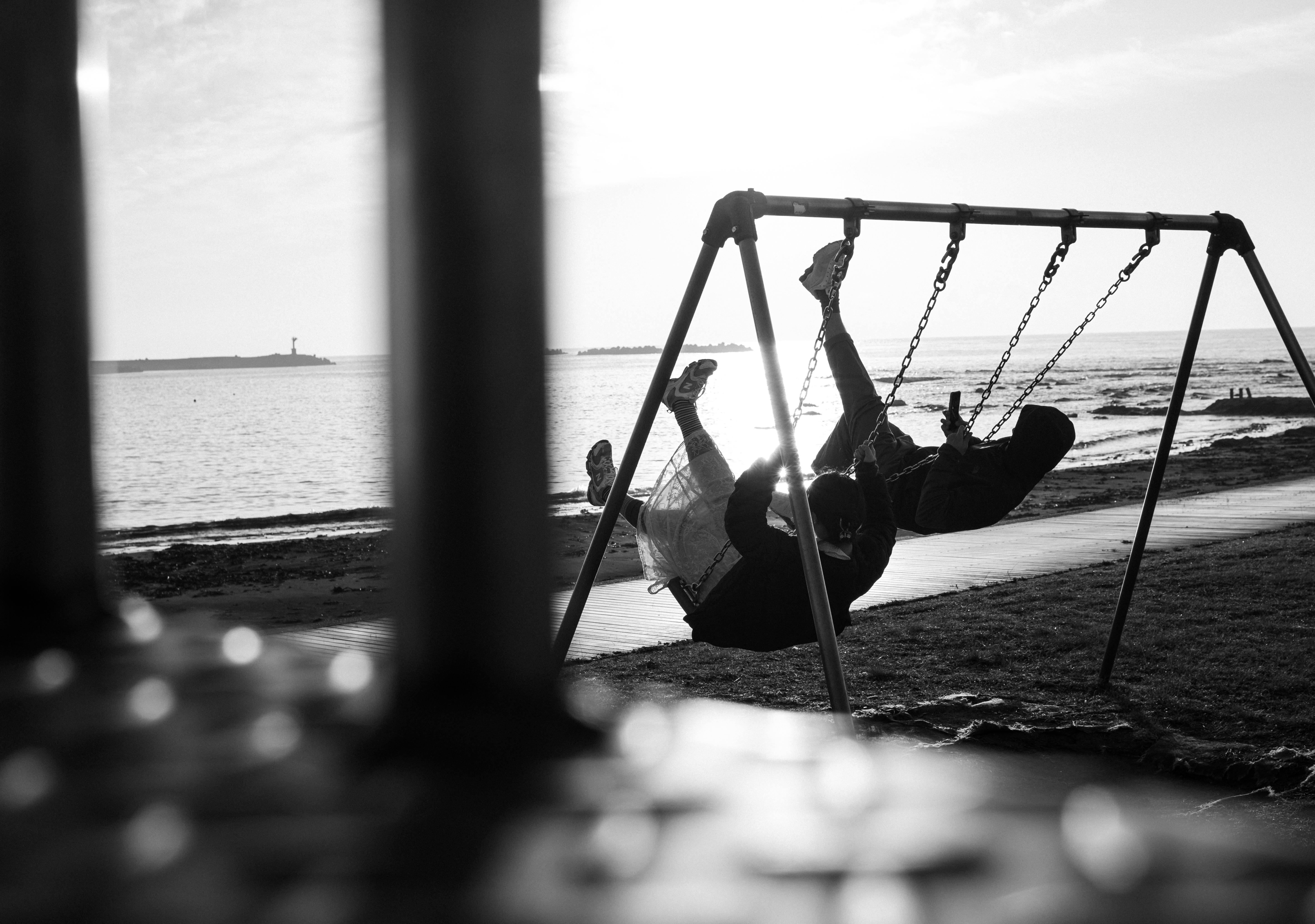 A couple enjoys swinging together by the seaside, capturing joyful moments in black and white