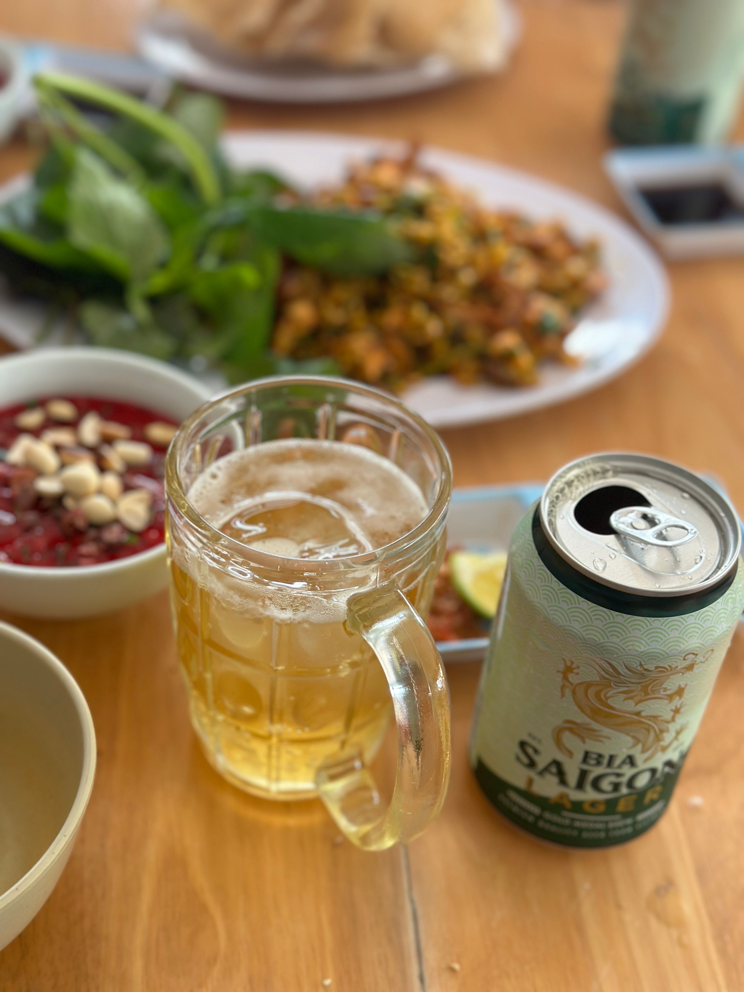Close-up of a Vietnamese meal with Saigon beer, peanuts, and greens.