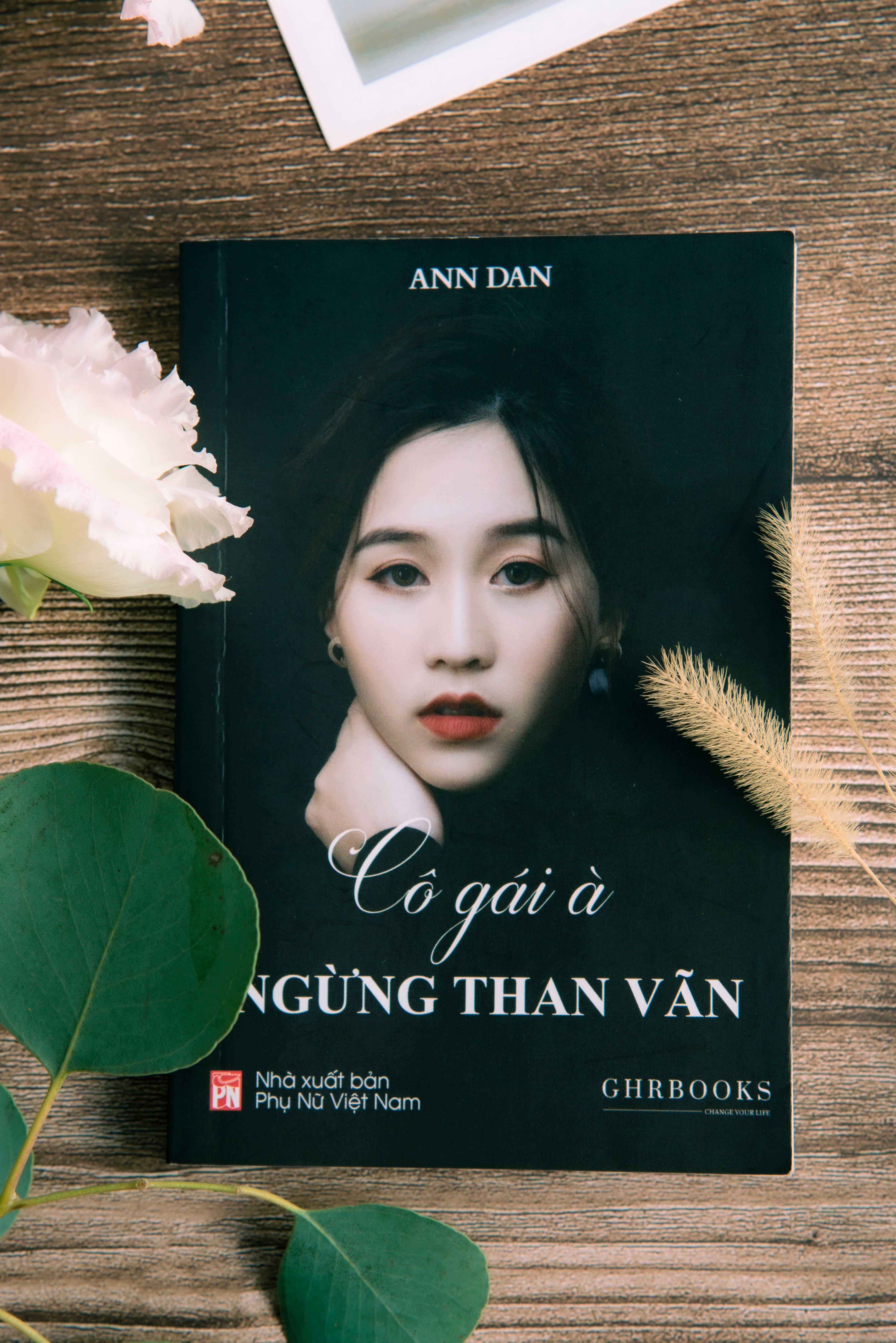 A Vietnamese book with a woman's portrait on a wooden table surrounded by flowers.