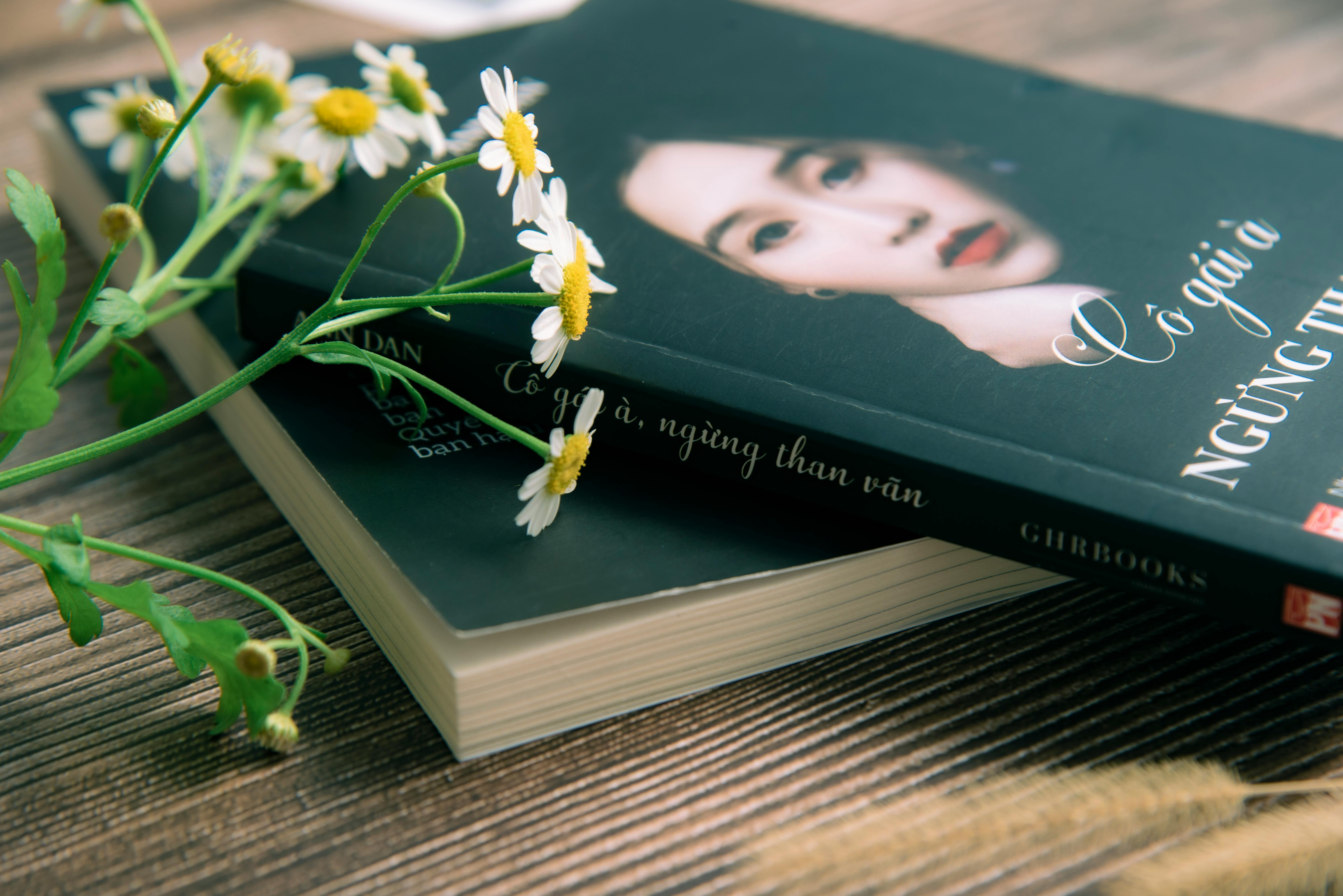 Close-up of a book with chamomile flowers on a wooden surface, conveying a peaceful reading atmosphere.