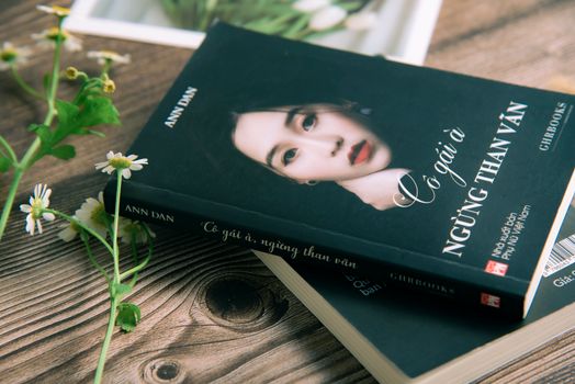 Close-up of a Vietnamese book cover with a portrait of a woman alongside daisies on a wooden table.