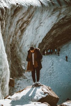 A lone individual stands on a snowy rock amidst a dramatic icy landscape in Almaty, Kazakhstan.