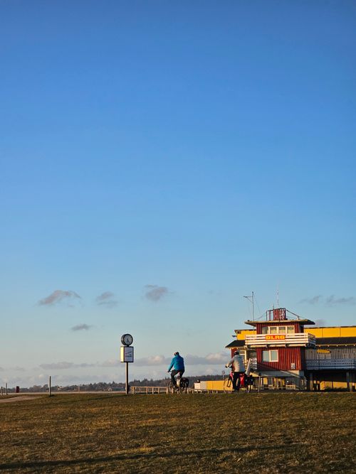 Free Scenic view of cyclists near a harbor building in Husum, Germany, under a clear blue sky. Stock Photo