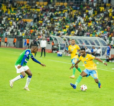 Players in action during a competitive football match at Kigali Stadium. Vibrant atmosphere and crowd.