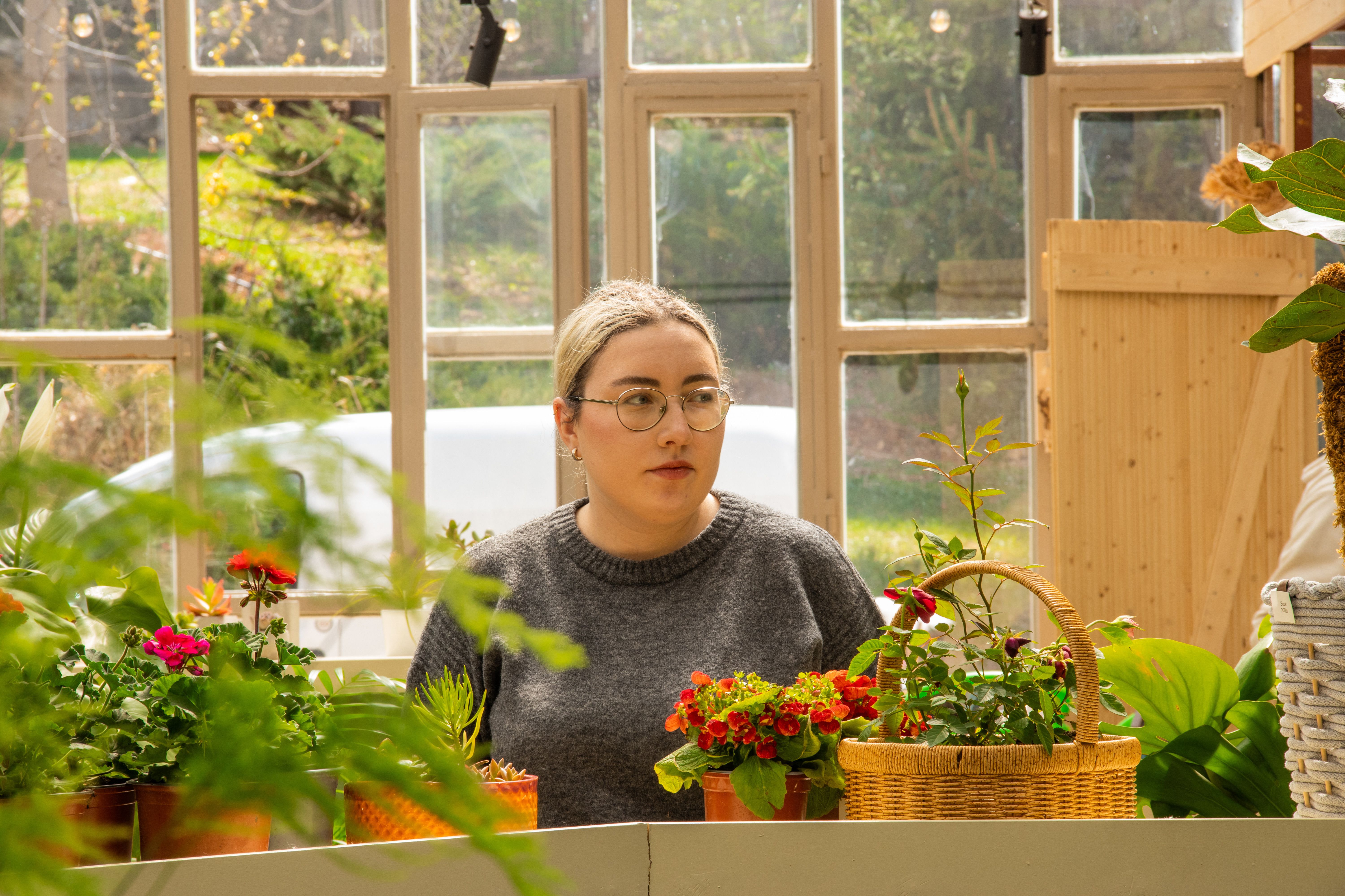 Woman in a cozy greenhouse setting with vibrant flowers, creating a serene atmosphere.