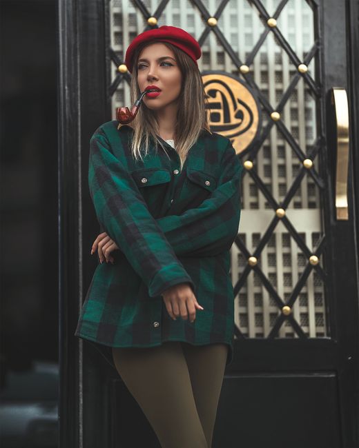 Stylish woman with a pipe exuding vintage street style in a red beret and checkered coat.