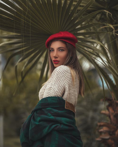 Foto De Foco Seletivo De Mulher Com Chapéu Vermelho Posando Sob Uma Folha De Palmeira