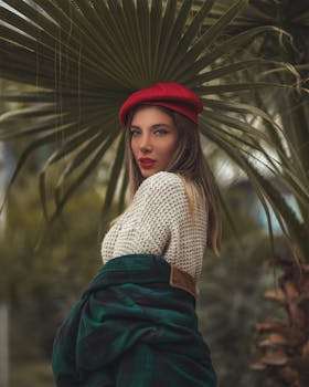 一位美丽的女子戴着红色贝雷帽，在户外以棕榈叶为背景摆姿势