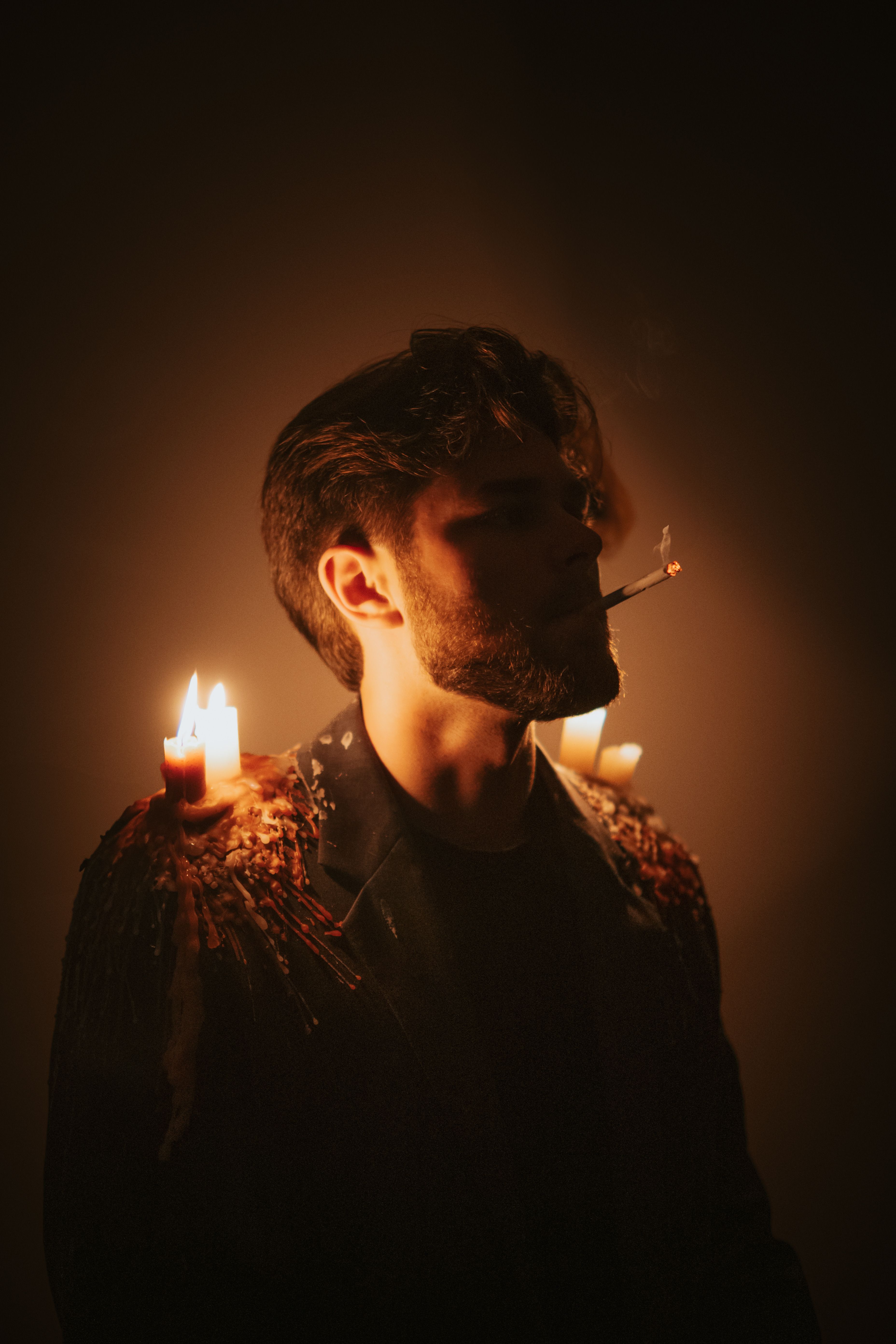 Atmospheric portrait of a man surrounded by burning candles, creating a moody ambiance.