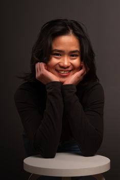 Charming portrait of a young woman in a black top, smiling with hands on her cheeks.