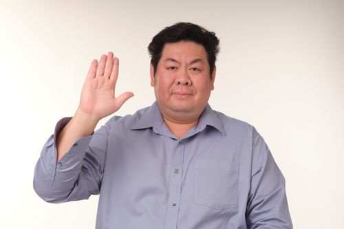 Free Man raises hand in a neutral indoor setting, expressing greeting or oath with confident demeanor. Stock Photo