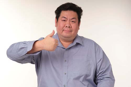 Free Smiling man in a blue shirt showing thumbs up against a plain background. Stock Photo