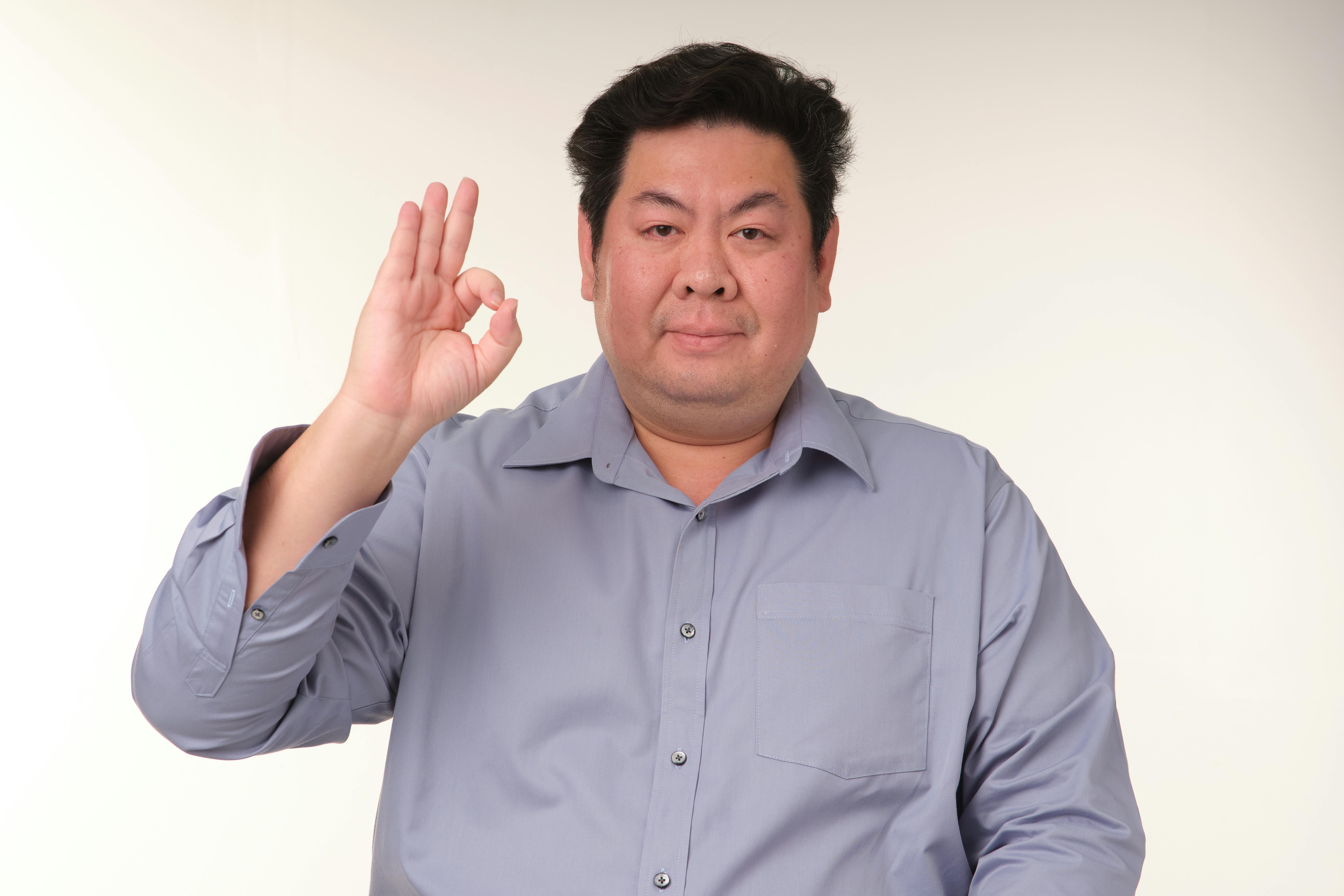 A man in a blue shirt making an 'ok' gesture against a neutral background, creating a calm and positive vibe.
