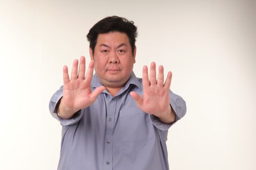 Free Serious man in blue shirt making stop gesture with both hands indoors against neutral background. Stock Photo