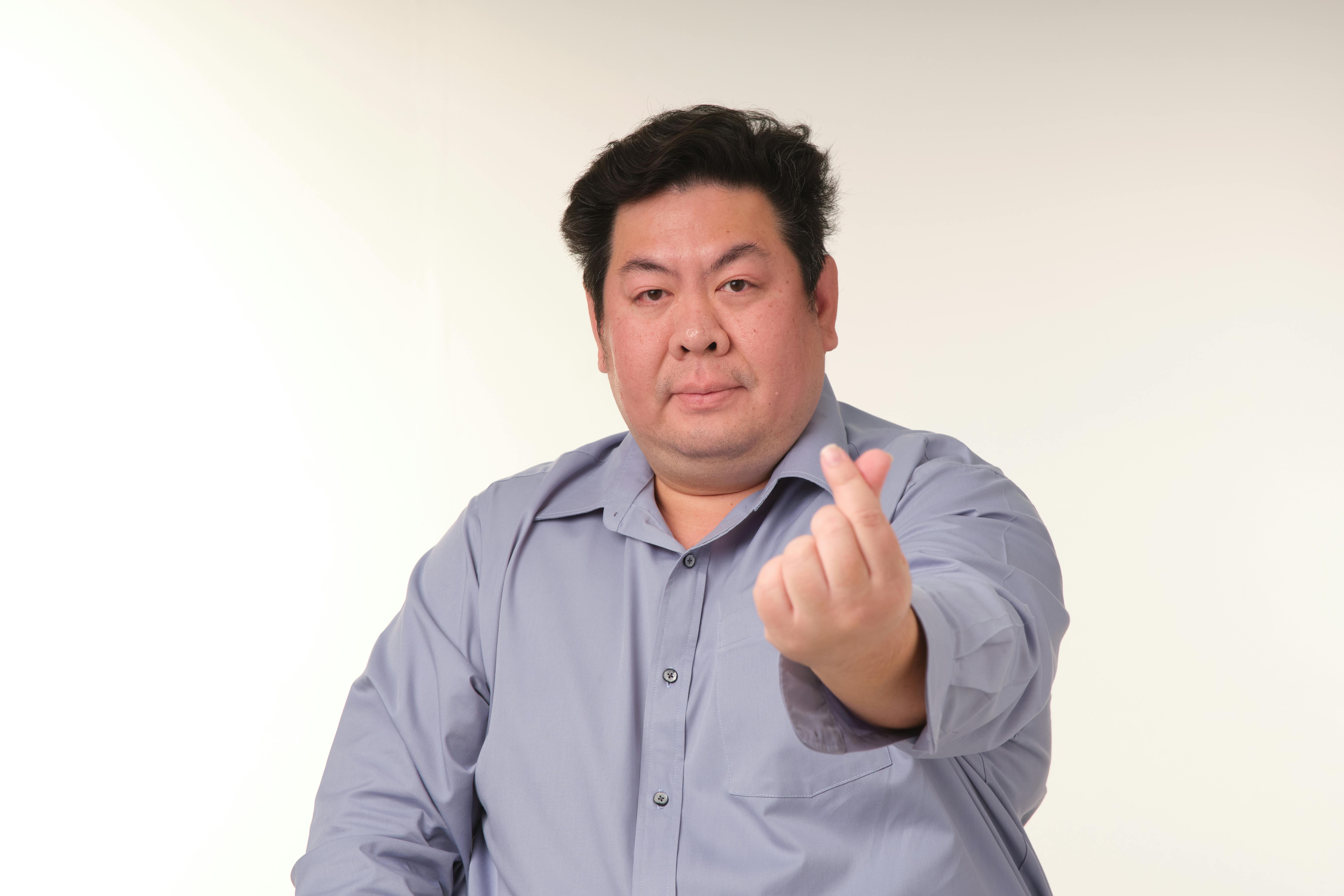 무료 스튜디오에서 파란색 셔츠를 입은 성인 남성이 손과 하트 제스처를 하고 있습니다. 스톡 사진