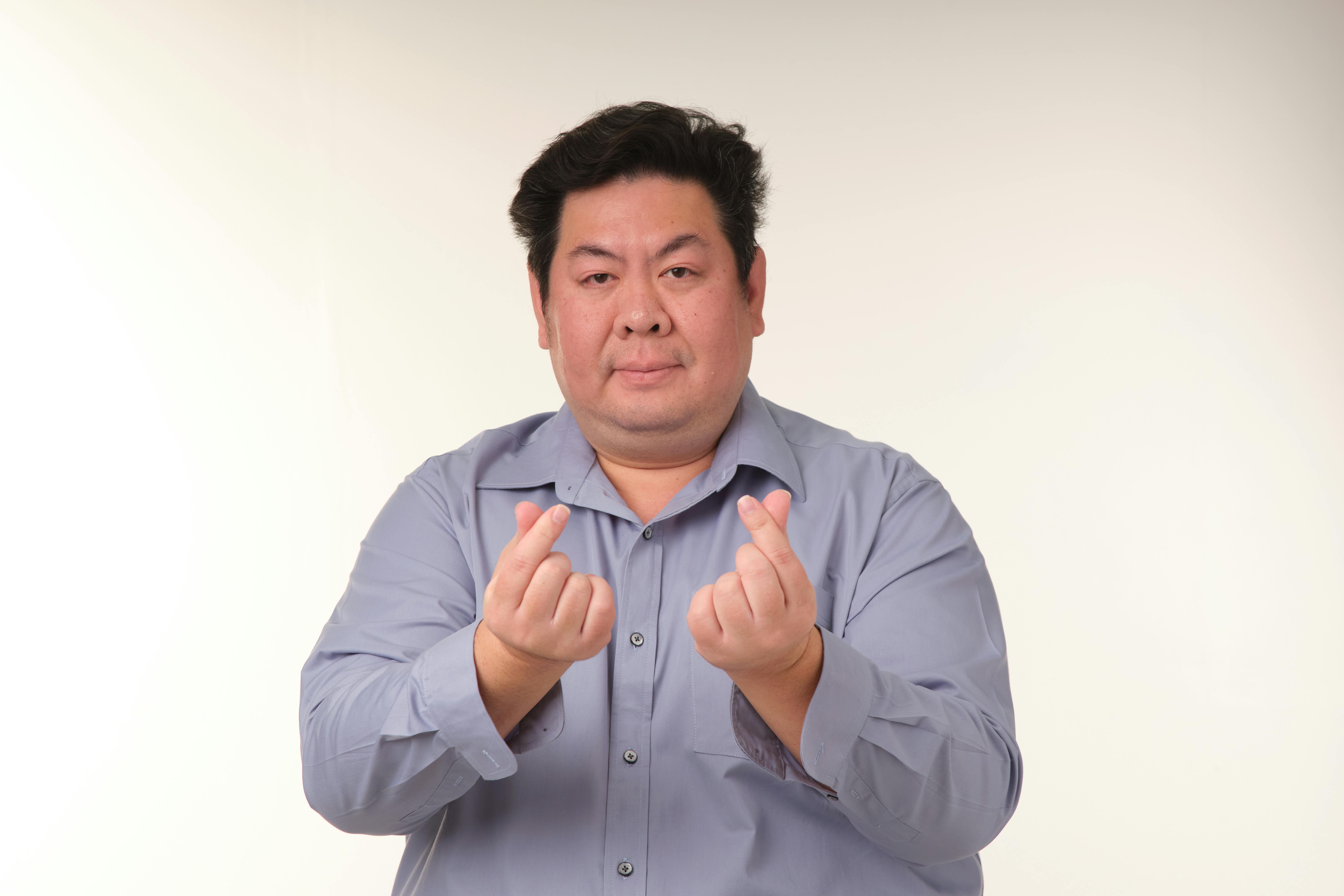Free Man making mini heart symbols with his hands, wearing a blue shirt in a studio setting. Stock Photo
