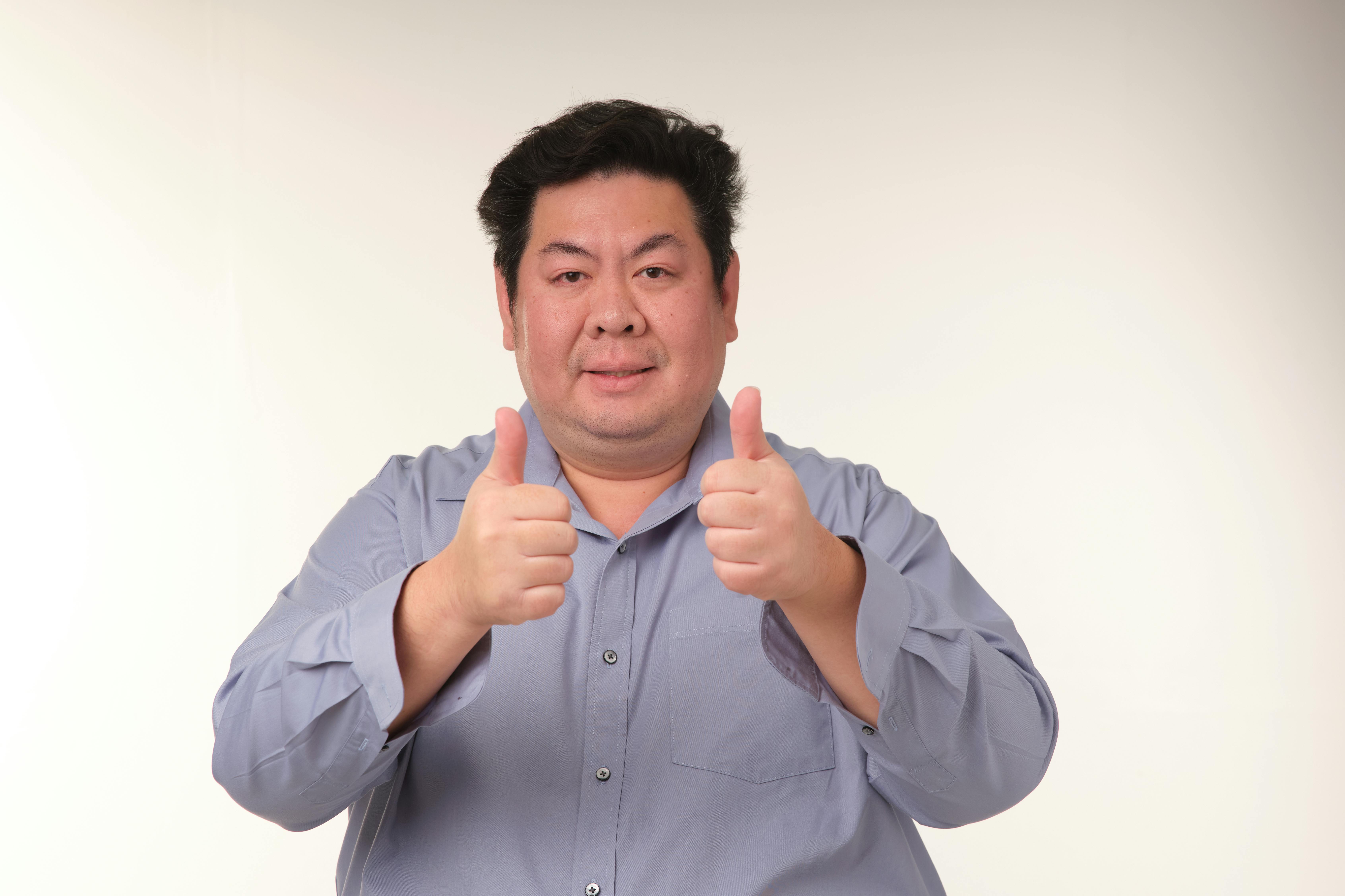 gratis Een vrolijke volwassen man in een blauw shirt die een dubbele duim omhoog geeft. Perfect voor concepten van goedkeuring en positiviteit. Stockfoto