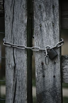 Weathered wooden gate secured with a rusty chain and padlock outdoors.