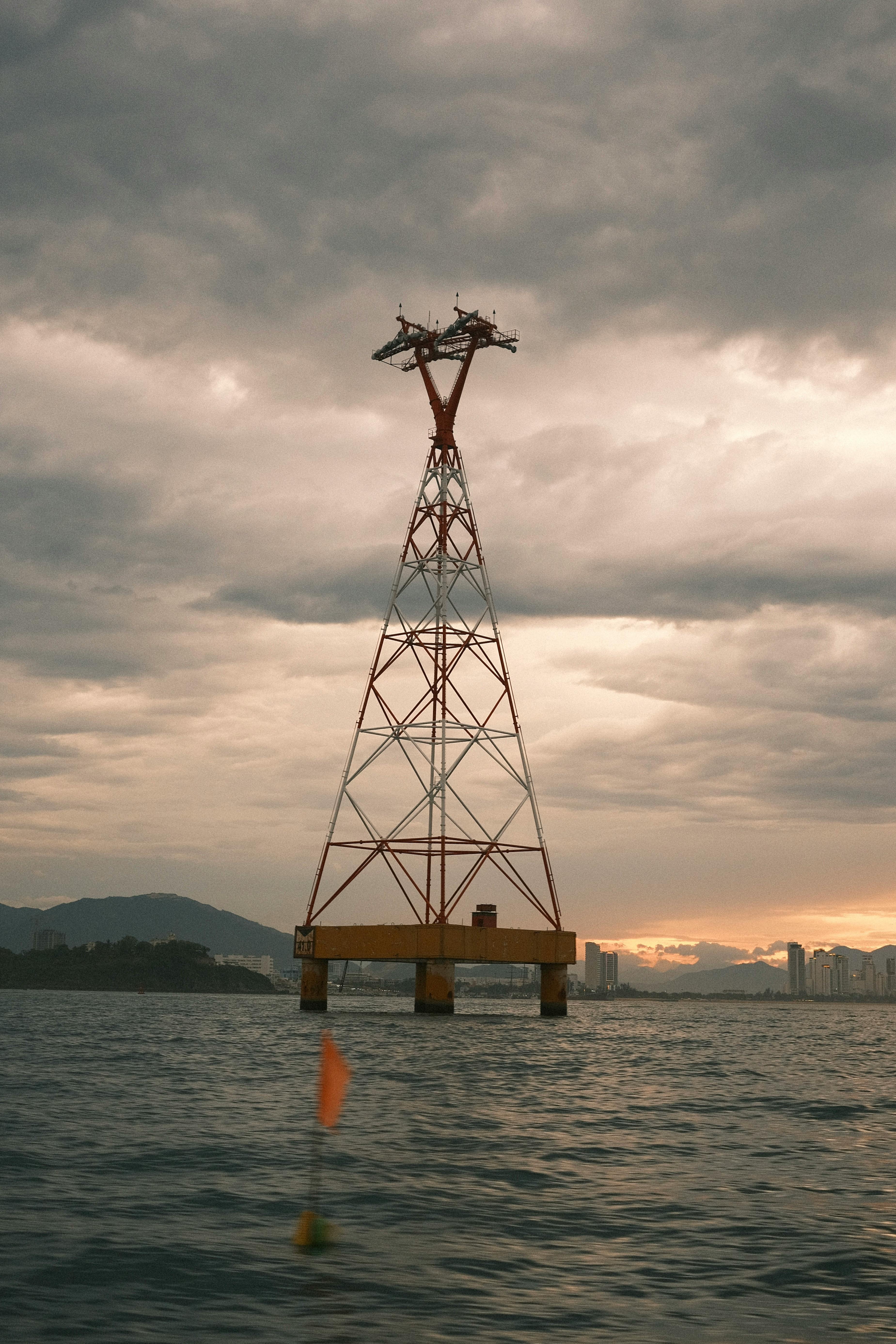 A tall electrical tower stands above a body of water during sunset with moody skies.