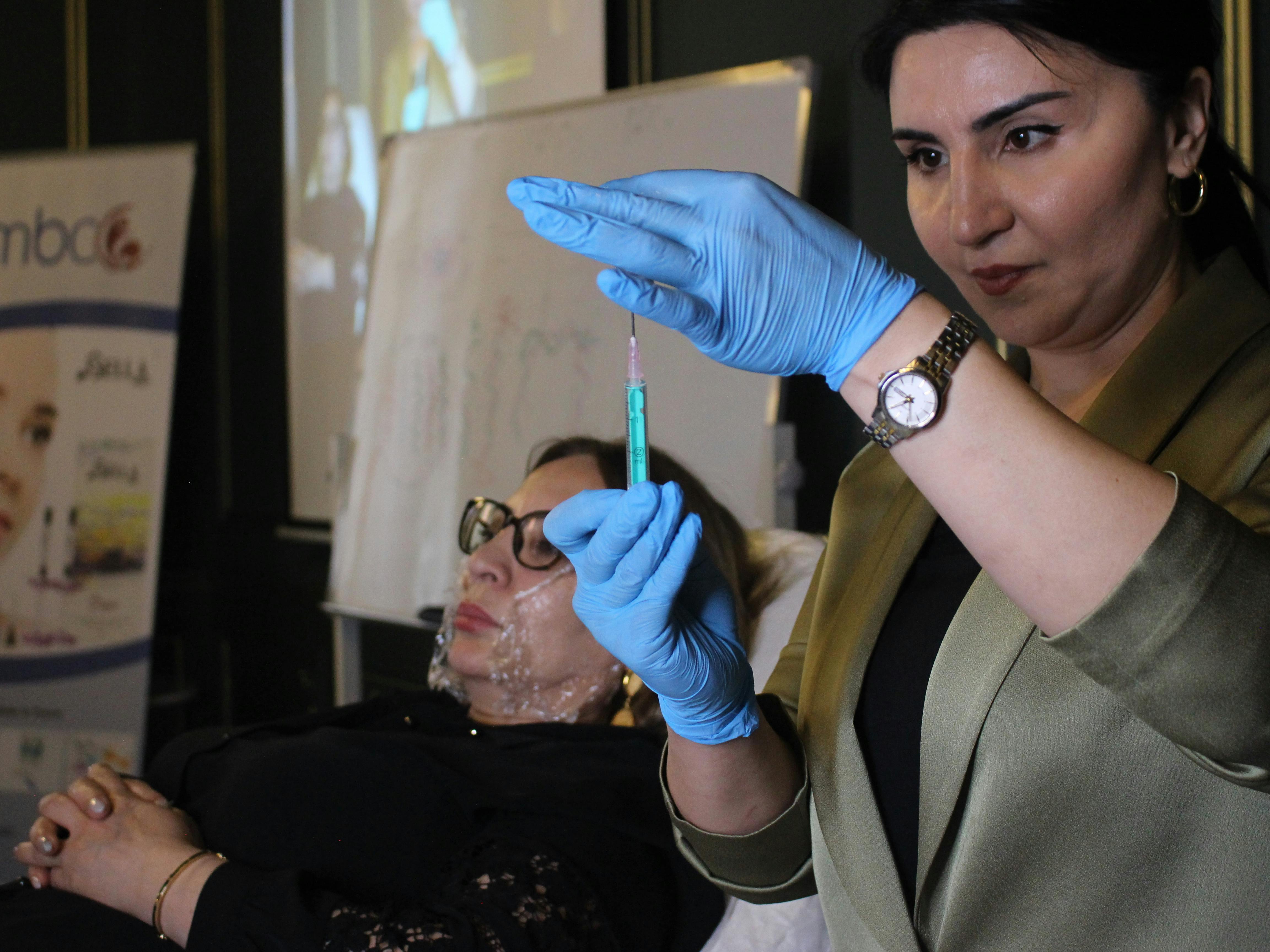 Free A professional demonstrates a cosmetic procedure using a syringe on a reclining patient. Stock Photo