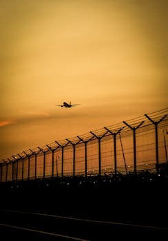 Silhouette of a plane taking off at sunset with airport fence in Jakarta. Dramatic sky creates a striking scene.