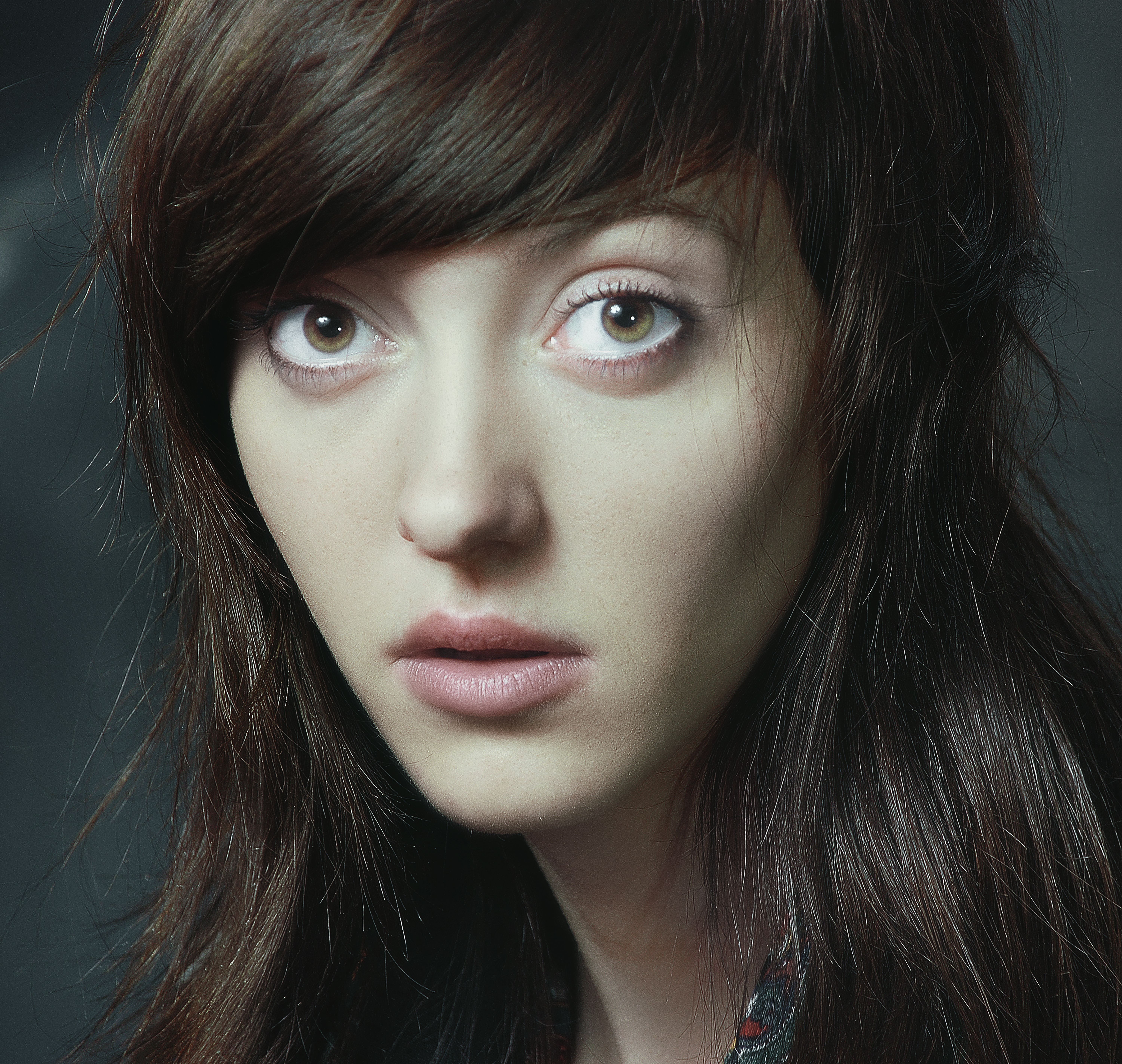 Close-up of a woman with intense gaze and dark hair, against a dark background.
