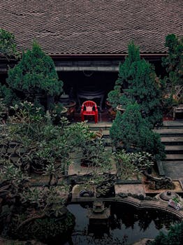 A tranquil courtyard scene featuring lush greenery and a striking red chair in Hanoi, Vietnam.
