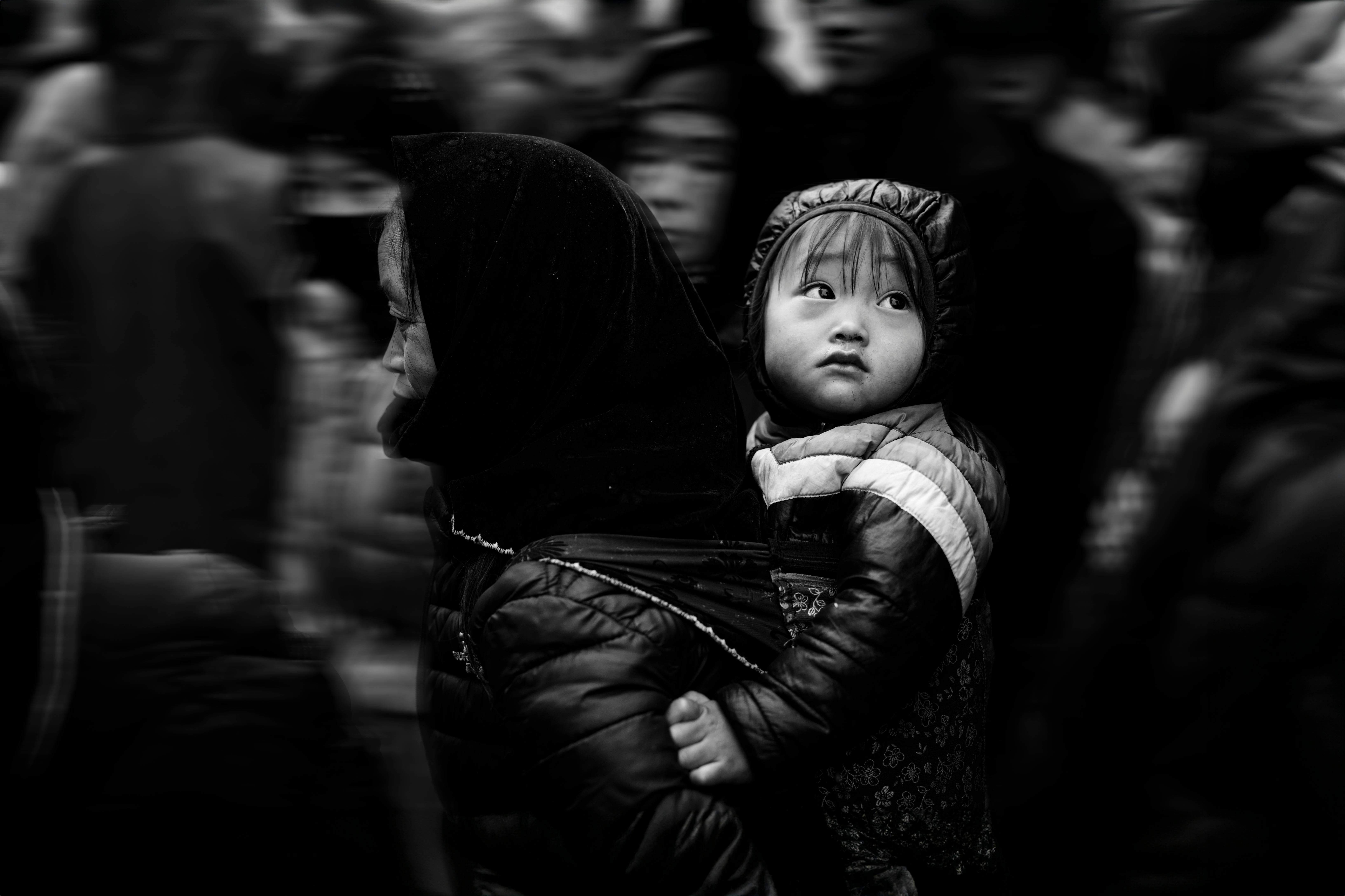 Captivating black and white street photo capturing a mother carrying her child through a bustling crowd.