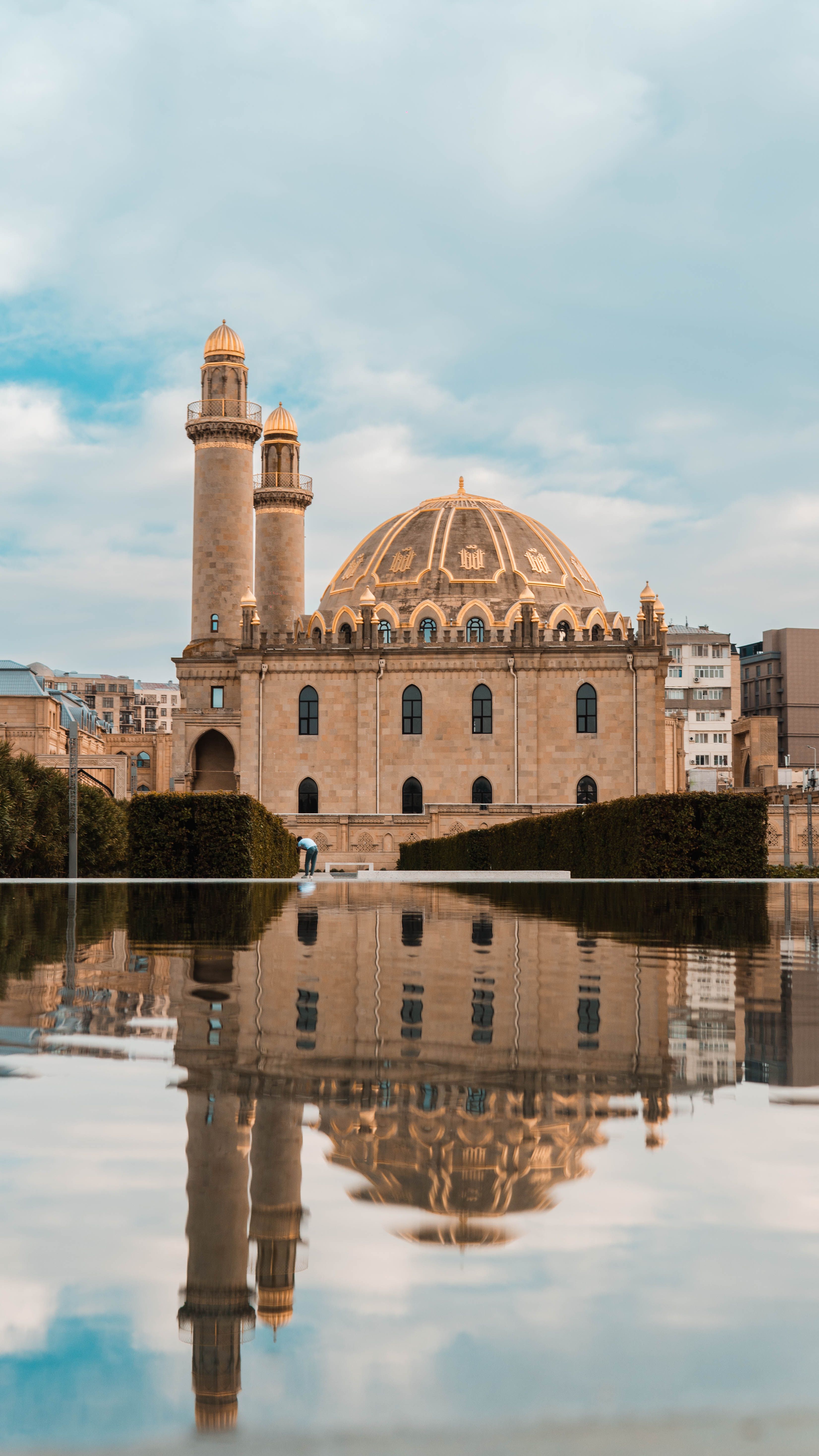 A picturesque mosque with twin minarets reflected in calm water beneath a clear sky.