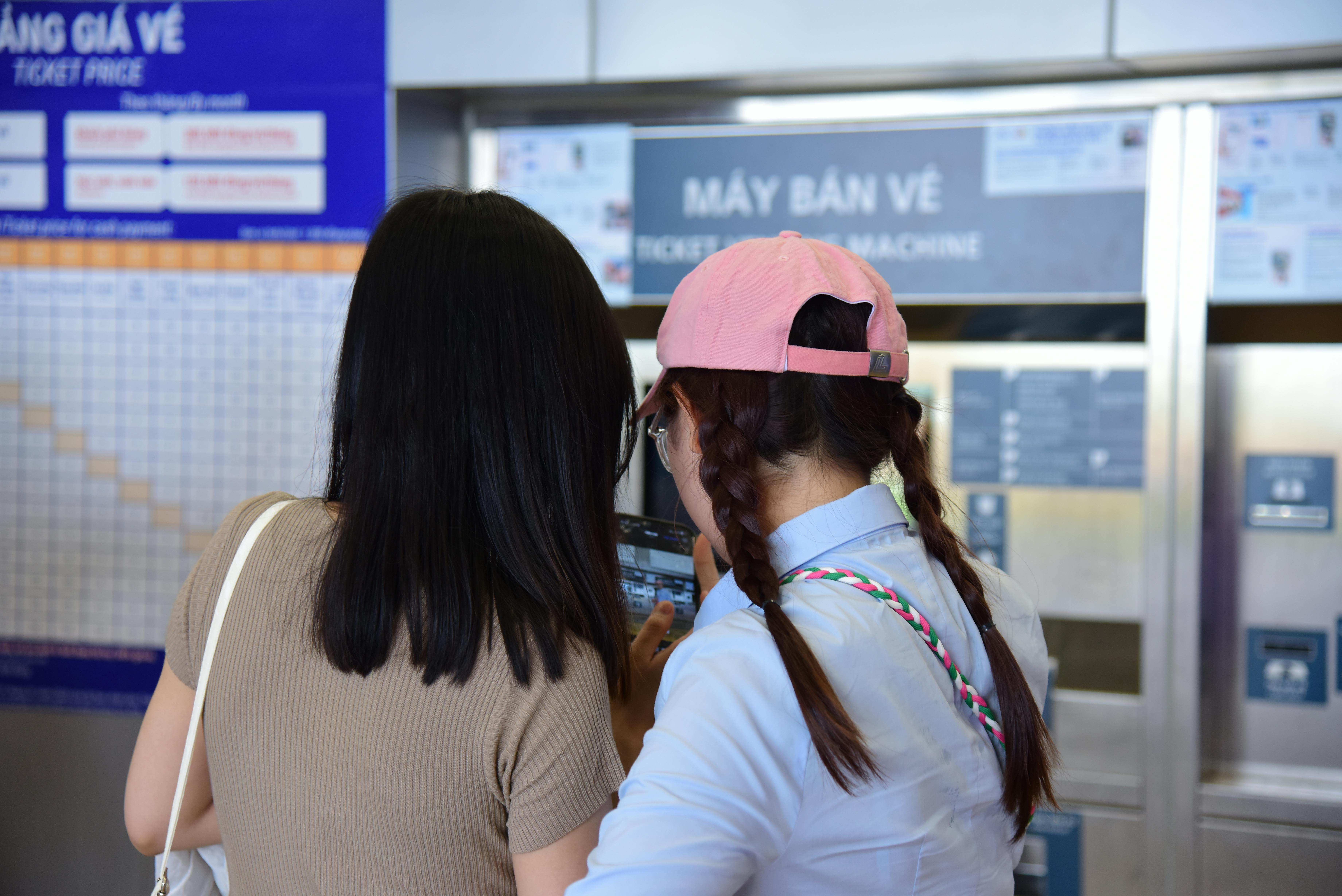 Two women purchasing tickets from a vending machine at a public transport station.