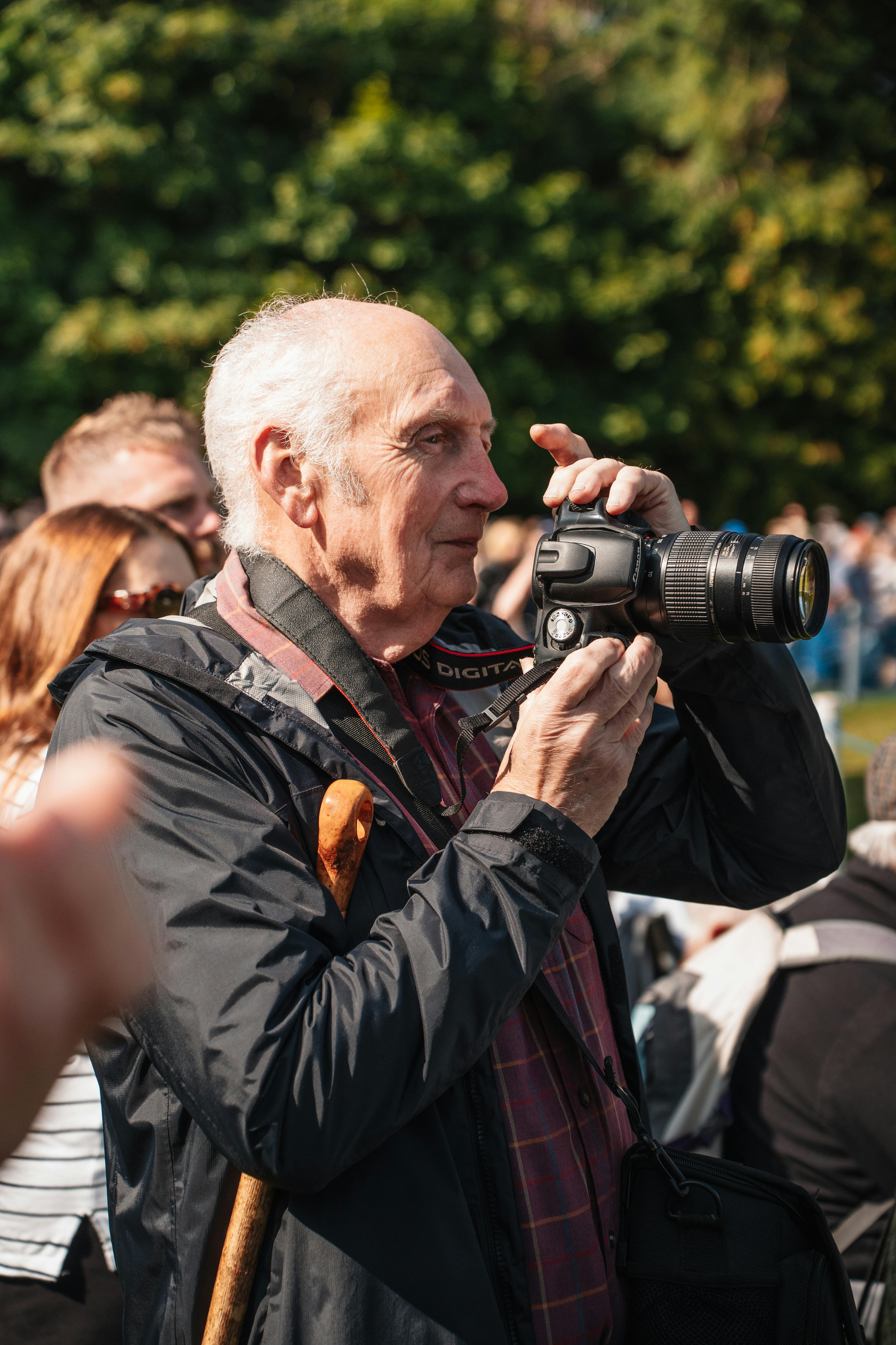 Senior male photographer with a camera capturing moments at an outdoor event in Scotland.