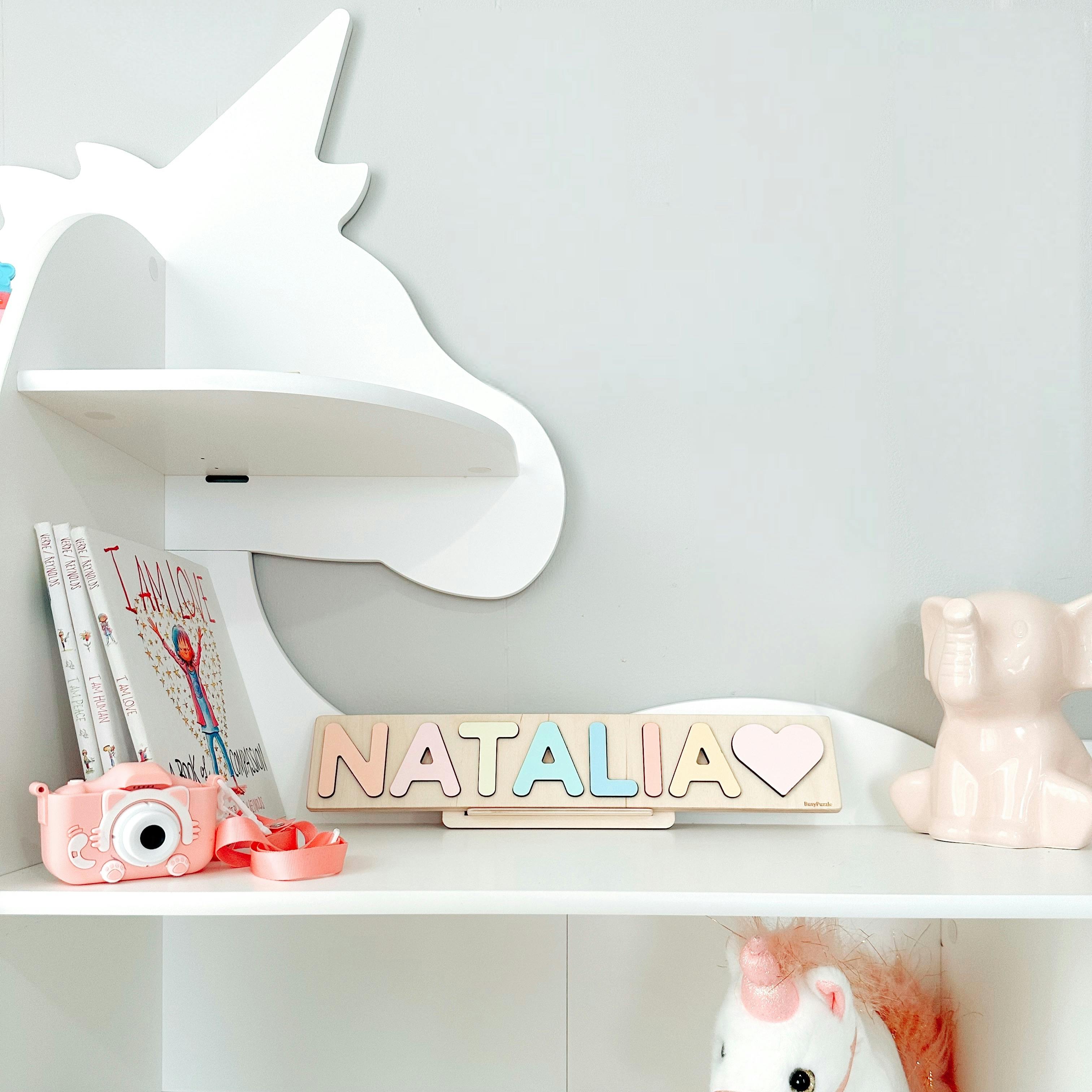 Charming child's room decor featuring unicorn shelves, pastel name sign, and toys.