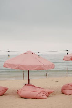 Serene beach scene with pink umbrellas and bean bags by the sea.