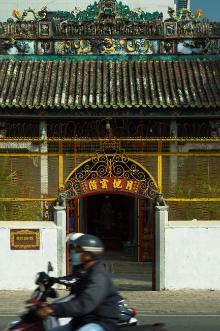 A motorcyclist drives by a traditional Asian temple gate with intricate designs.